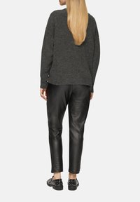 Dunkelgrauer oversized Strickpullover mit überschnittenen Schultern, kombiniert mit schwarzen Lederhosen und verzierten Slippern.