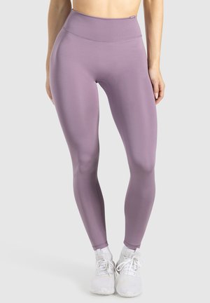 Paarse hoog- taille legging van rekbaar materiaal, met een gladde textuur en aansluitend ontwerp. Witte sportschoenen maken de look af.
