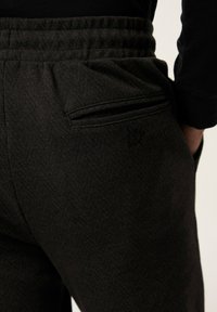 Pantalones jogger de houndstooth negro con cintura elástica, que cuentan con un bolsillo con cremallera en la parte posterior y un logo sutil impreso en la tela.