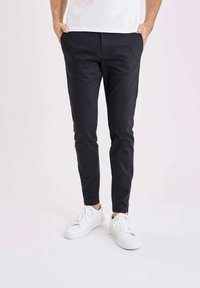 Schwarze Slim-Fit-Hosen aus glattem Stoff, mit Seitentaschen und einem schlichten Design, kombiniert mit weißen Sneakers.