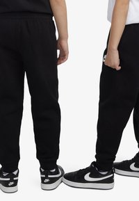 Čierne tepláky s elastickým pásom a zakončením na členkoch; kombinované s čiernymi teniskami s bielym logom Nike.