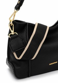 Mustast nahast käekott tekstuurse viimistlusega, millel on kuldse tooniga kinnitus ja eemaldatav rihm beežikirju detailiga.