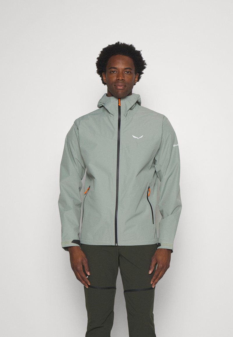 Veste imperméable gris clair avec capuche ajustable, zips orange et poches latérales noires. Présente un design élégant et moderne.