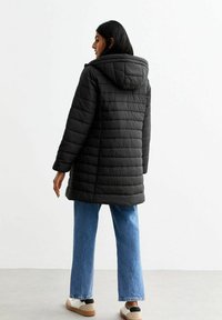 Zwarte pufferjack met een capuchon, gewatteerd ontwerp en een middellange snit. Gecombineerd met lichtblauwe wijde jeans en neutrale sneakers.