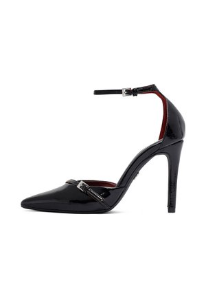 Zapato de tacón alto de charol negro con puntera puntiaguda, correa en el tobillo y correa decorativa con hebilla en la parte delantera.