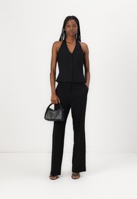 Černý halter top s jemnými ozdobami, doplněný o černé kalhoty na míru. Modelka drží malou černou kabelku a má na sobě sandály na podpatku.