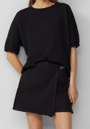 T-shirt noir à manches courtes avec une coupe décontractée, associé à une jupe en denim noire avec un design enveloppant et un détail en chaîne métallique à la taille.