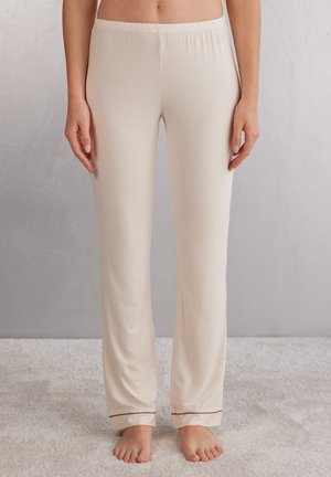 Beige Lounge-Hosen mit elastischem Bund, glatter Textur und kontrastierendem Besatz am Knöchel. Figurbetont und leicht ausgestellt.