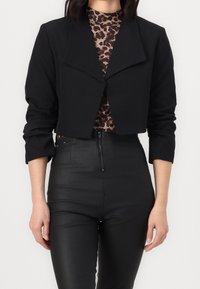 Svart kort blazer med en bred krage och långa ärmar, tillsammans med en topp i leopardmönster och högmidjade svarta byxor. Slät textur.