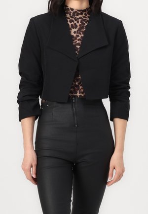 Svart kort blazer med en bred krage och långa ärmar, tillsammans med en topp i leopardmönster och högmidjade svarta byxor. Slät textur.