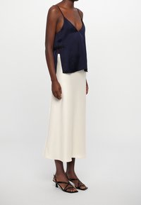 Camisole en satin marine avec fentes sur les côtés, associé à une jupe droite en satin crème et des talons noirs à lanières. Texture lisse et design fluide.