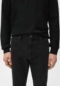 Vaqueros negros con diseño ajustado, cinco bolsillos y cierre de botón, combinados con una camiseta negra de manga larga con cuello acanalado.