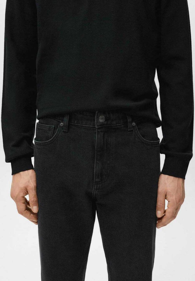 Jean noir à coupe ajustée, cinq poches, fermeture par bouton, associé à un t-shirt noir à manches longues avec un col côtelé.