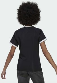 Svart kortärmad skjorta med vit krage och ärmkanter, med en slät yta och en avslappnad passform, sedd bakifrån.