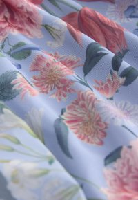 Tissu bleu clair avec des fleurs roses et blanches détaillées et des feuilles vertes dans un tissage doux et texturé avec des plis délicats.