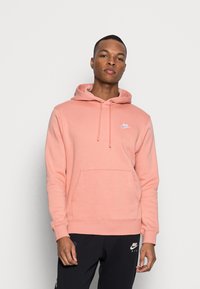 Felpa rosa chiaro con tasca frontale, coulisse e un piccolo logo bianco Nike sul petto. Materiale in cotone morbido, vestibilità regolare.