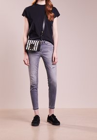 Camisa negra de manga corta, jeans ligeros de color gris desgastado, deportivas de ante negras, llevando un bolso bandolera a rayas en blanco y negro con un cierre metálico.