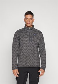 Fleece pullover with a half-zip, featuring a gray zigzag pattern, high collar, and chest pocket. Textured fabric with a soft finish.