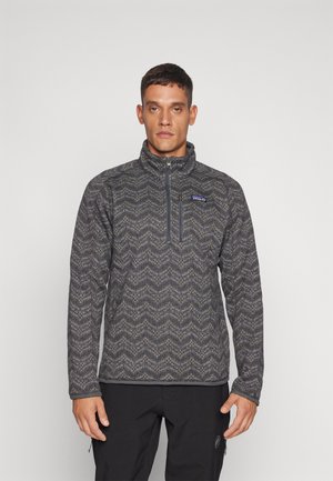 Sudadera de forro polar con media cremallera, presenta un patrón en zigzag gris, cuello alto y bolsillo en el pecho. Tejido texturizado con un acabado suave.