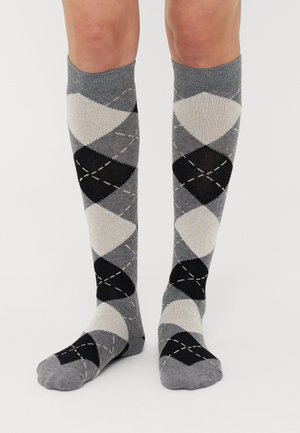 Kniestrümpfe mit einem Argyle-Muster in Hellgrau, Dunkelgrau und Schwarz, verziert mit kontrastierenden Stichen. Hergestellt aus einem weichen, dehnbaren Material.