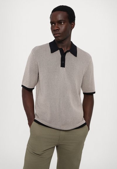 Strikket polo skjorte i beige med teksturdesign, svart krage og matchende ermer. Brukt med olivengrønne bukser.