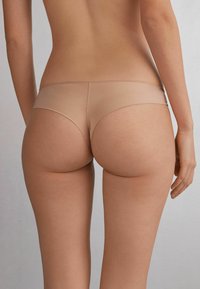Culottes couleur chair avec un design lisse et sans coutures. Fabriquées en matériau extensible, elles présentent une taille basse et une couverture minimale.