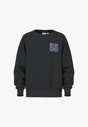 Schwarzer Pullover mit Raglanärmeln, mit einer strukturierten "86" Applikation auf der linken Brust. Weicher Stoff, gerippte Bündchen und Saum.