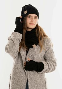 Zwarte gebreide muts, sjaal en handschoenen zonder vingers. Zachte textuur, geribbeld ontwerp, met een leren label op de sjaal. Gedragen bij een grijze jas.