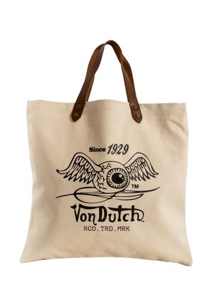 Sac fourre-tout en toile beige avec des poignées en cuir marron, arborant un dessin noir d’un globe oculaire ailé et le texte « Von Dutch Since 1929 ».