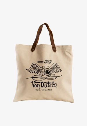 Bolsa tote de lona beige con asas de cuero marrón que presenta un gráfico negro de un globo ocular alado y el texto "Von Dutch Since 1929".