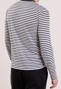 Långärmad tröja med svartvita horisontella ränder, rund halsringning och en mjuk bomullstextur. Bakgrunden visar ärmlängd och passform.