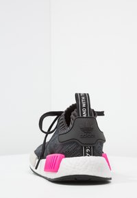 Svart stickad träningssko med rosa accenter och vit mellansula, med en texturerad ovandel, svarta snören och en märkeslogga på hälen.