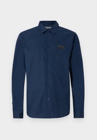 Camicia a maniche lunghe blu navy in cotone, con colletto button-down, bottoni frontali e una patch con logo sul petto.