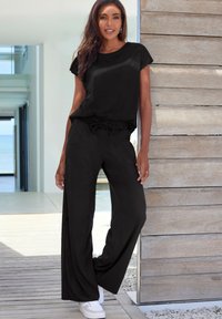 Black, short-sleeve top and wide-legged pants made from a smooth fabric, complemented by white sneakers and a drawstring waistband detail.
