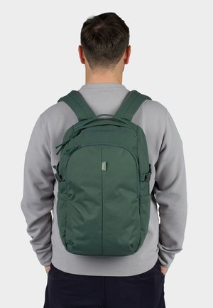 Green backpack with adjustable straps, multiple zippered compartments, a smooth fabric texture, and a logo patch on the front.