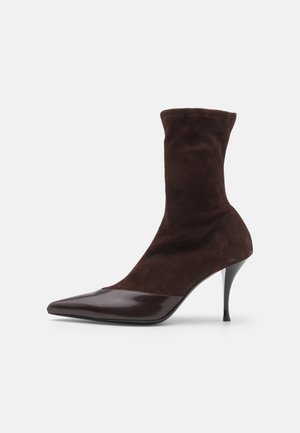 Kohvpruun nahast pahkluu saabas, millel on terav nina ja läikiv burgundia punane laki ninaosa, koos peene stiletto kontsaga ja tekstuurse ülemise osaga.