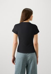 T-shirt nera a righe con maniche corte, design aderente, scollatura rotonda e una texture liscia. Indossata con pantaloni in denim a gamba larga di un blu chiaro.