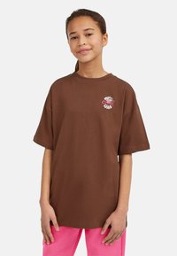 Brun oversize t-shirt med rund halsringning och korta ärmar, med en färgglad grafisk design på bröstet. Slät bomullstextur.