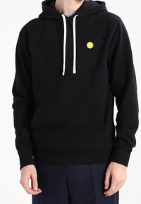 Black hooded sweatshirt with a front pocket, white drawstrings, and a small yellow logo on the chest. Soft fabric and relaxed fit.