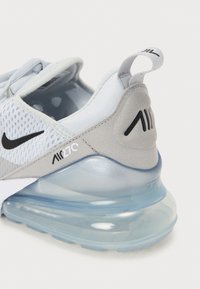 Szürke és fehér sneaker, hálós és szintetikus anyagból, átlátszó légpárnázással, fekete logókkal a saroknál és az oldalon.