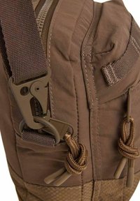 Bolsa de tela marrón con acentos texturizados, que cuenta con un zipper resistente, bordes acolchados y correas ajustables con clips y detalles de nudos.