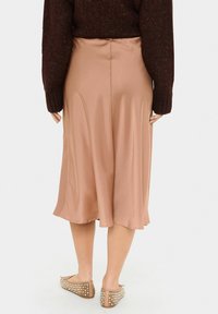Brown knit sweater paired with a knee-length, satin, pale pink skirt. The skirt has a smooth texture and a slight flare at the hem.