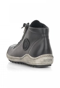 Bottine en cuir noir avec fermeture éclair, bout rond et semelle grise texturée. Présente un patch logo sur le côté et des accents de double couture.