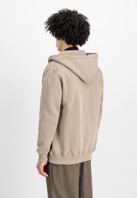 Sudadera con capucha beige, con puños y dobladillo de canalé, que presenta un ajuste relajado y una textura suave y lisa. La vista trasera resalta la capucha y los detalles de las costuras.