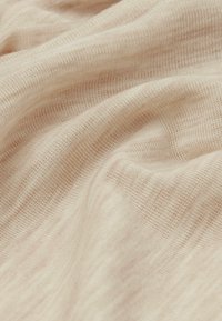 Helles beige Gewebe mit einer weichen, strukturierten Webart, die subtile Farb- und Musterabweichungen aufweist, in sanften Falten drapiert.