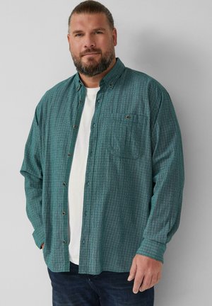 Green checkered shirt with long sleeves, button-front design, and chest pocket, layered over a white T-shirt, paired with dark jeans.