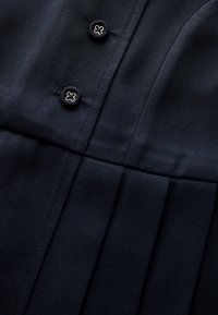 Marineblaues, plissiertes Gewebe mit zwei metallischen, blumenförmigen Knöpfen. Das Material hat eine feine Textur und eine glatte Oberfläche.