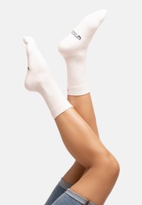 White cotton socks with ribbed texture, featuring a logo on the upper side and a contrasting red accent near the ankle.