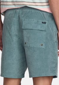 Shorts en velours côtelé teal avec une poche arrière, arborant une petite étiquette RVCA. Texture lisse et coupe décontractée, avec une ceinture élastique.