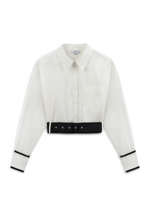 White cropped shirt with a collar, long sleeves, a front pocket, and black belt detail at the waist with eyelet accents. Black stripe at sleeve cuffs.